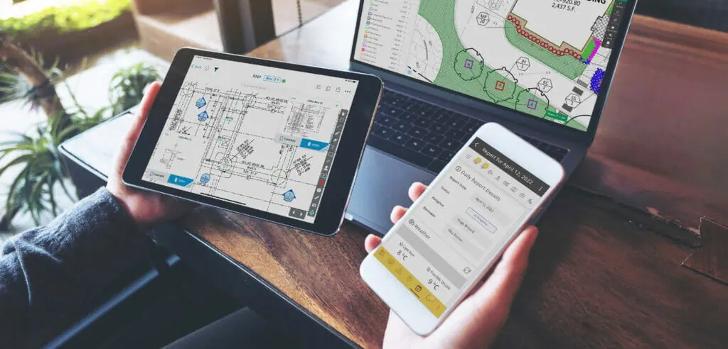 En un escritorio, alguien sostiene un iPad en la mano izquierda, que muestra una pantalla SmartUse, y un iphone en la mano derecha, que muestra una pantalla K-Ops. Un Macbook al fondo muestra una pantalla STACK .